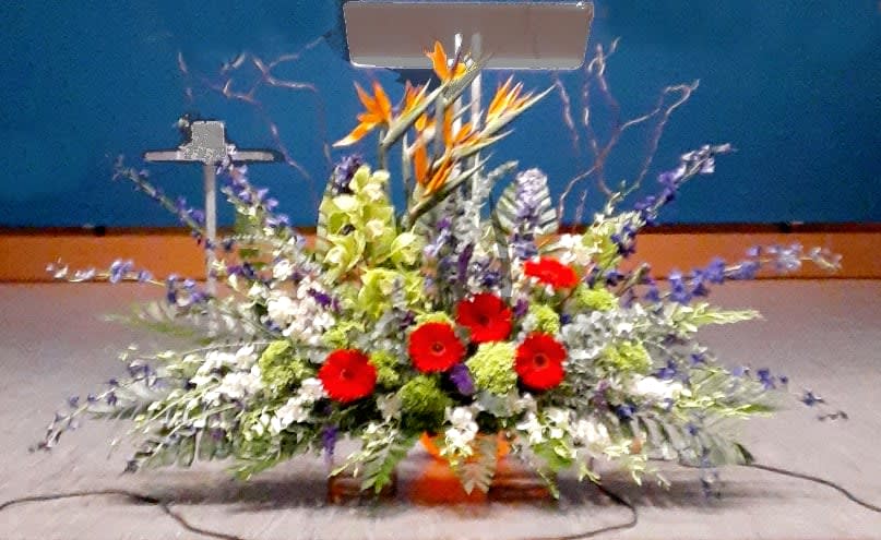 Large altar arrangement with red gerberas, orange birds of paradise, and purple flowers in a low container