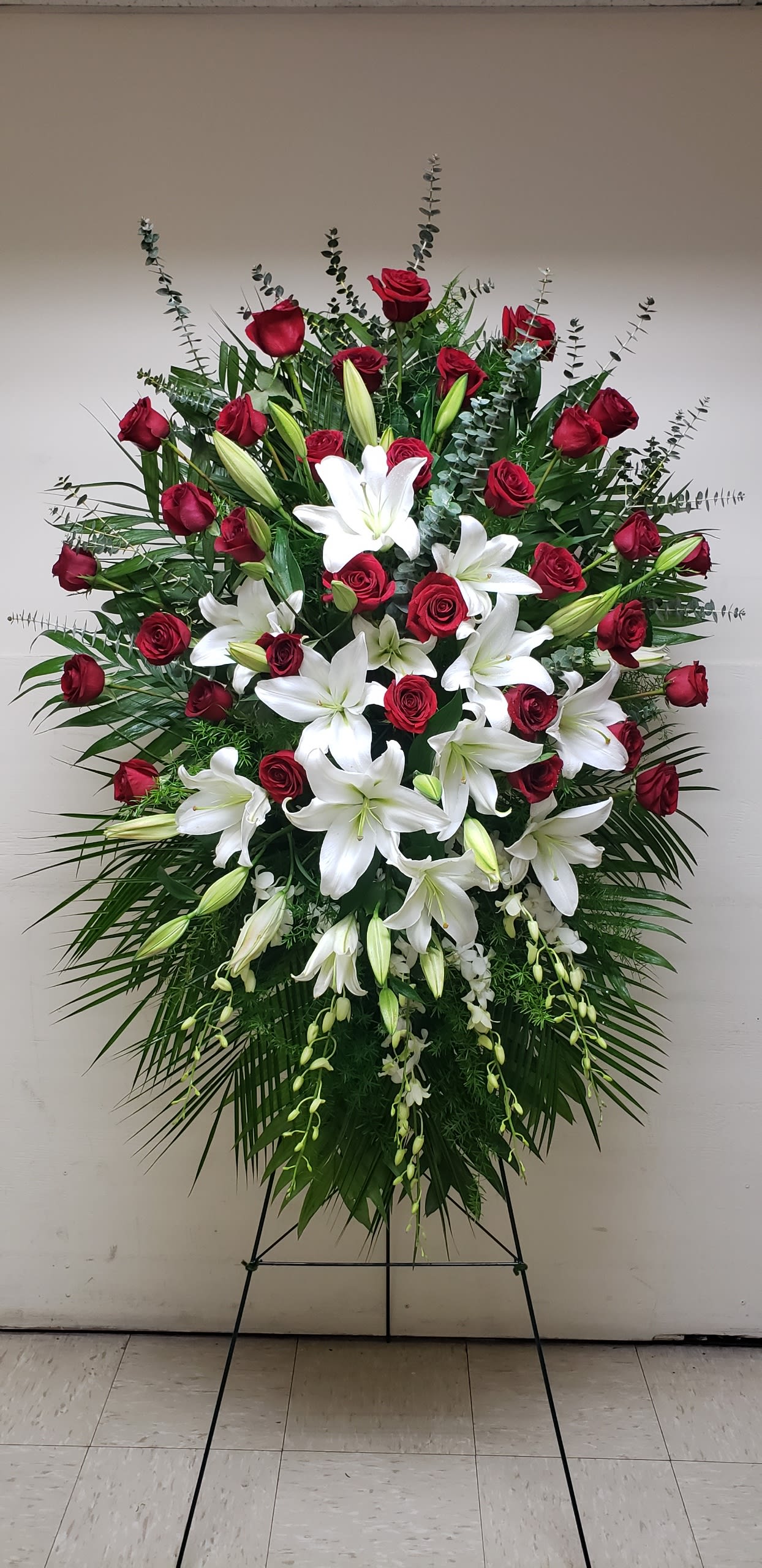 Standing floral spray with red roses and white lilies on an easel