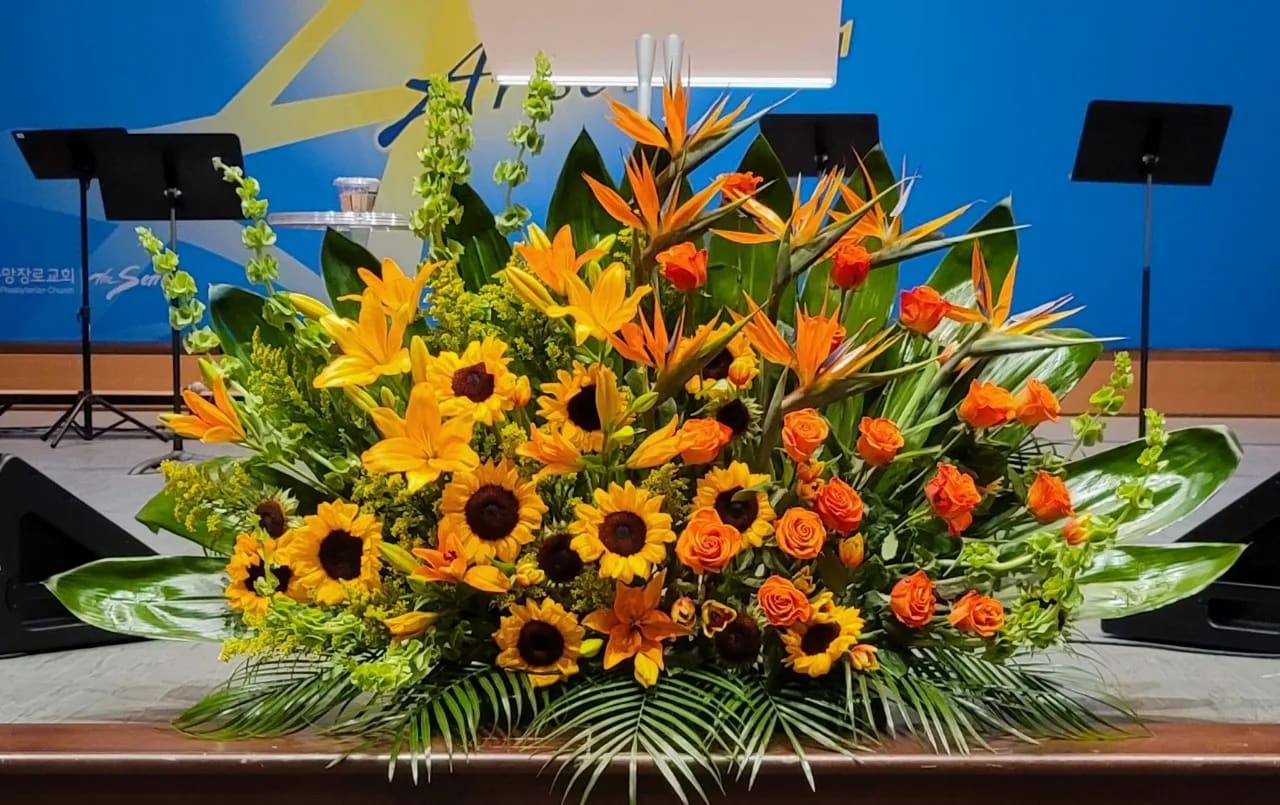 Large yellow and orange altar-style flower arrangement with sunflowers, lilies, roses, and birds of paradise.