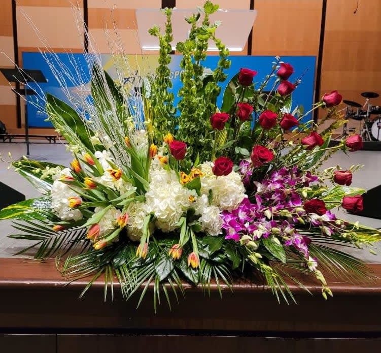 Large altar-style arrangement with red roses, white hydrangeas, orchids, tulips, and tall green spikes.
