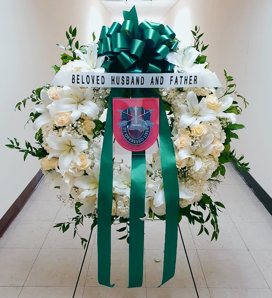 White funeral wreath with lilies, roses, and a green ribbon bow