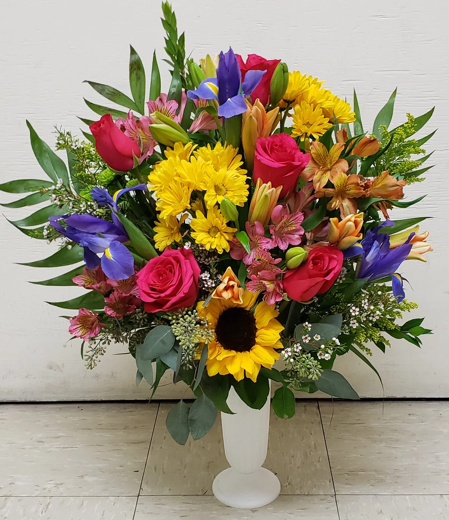 Colorful mixed bouquet in a white pedestal vase with roses, sunflowers, and irises