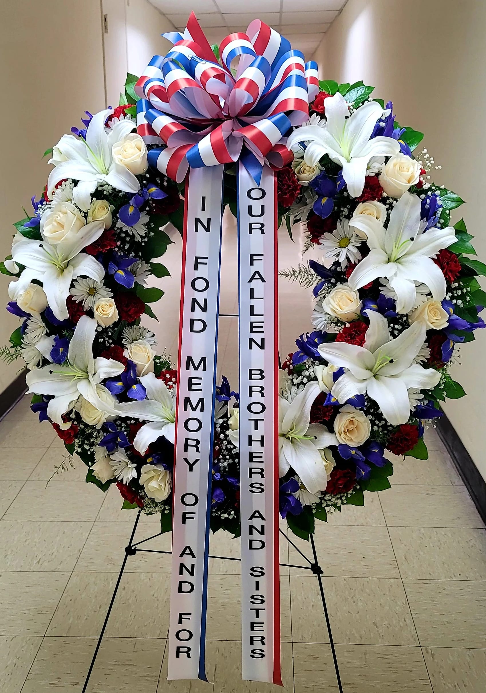Large memorial wreath with white lilies, roses, and blue flowers on a stand