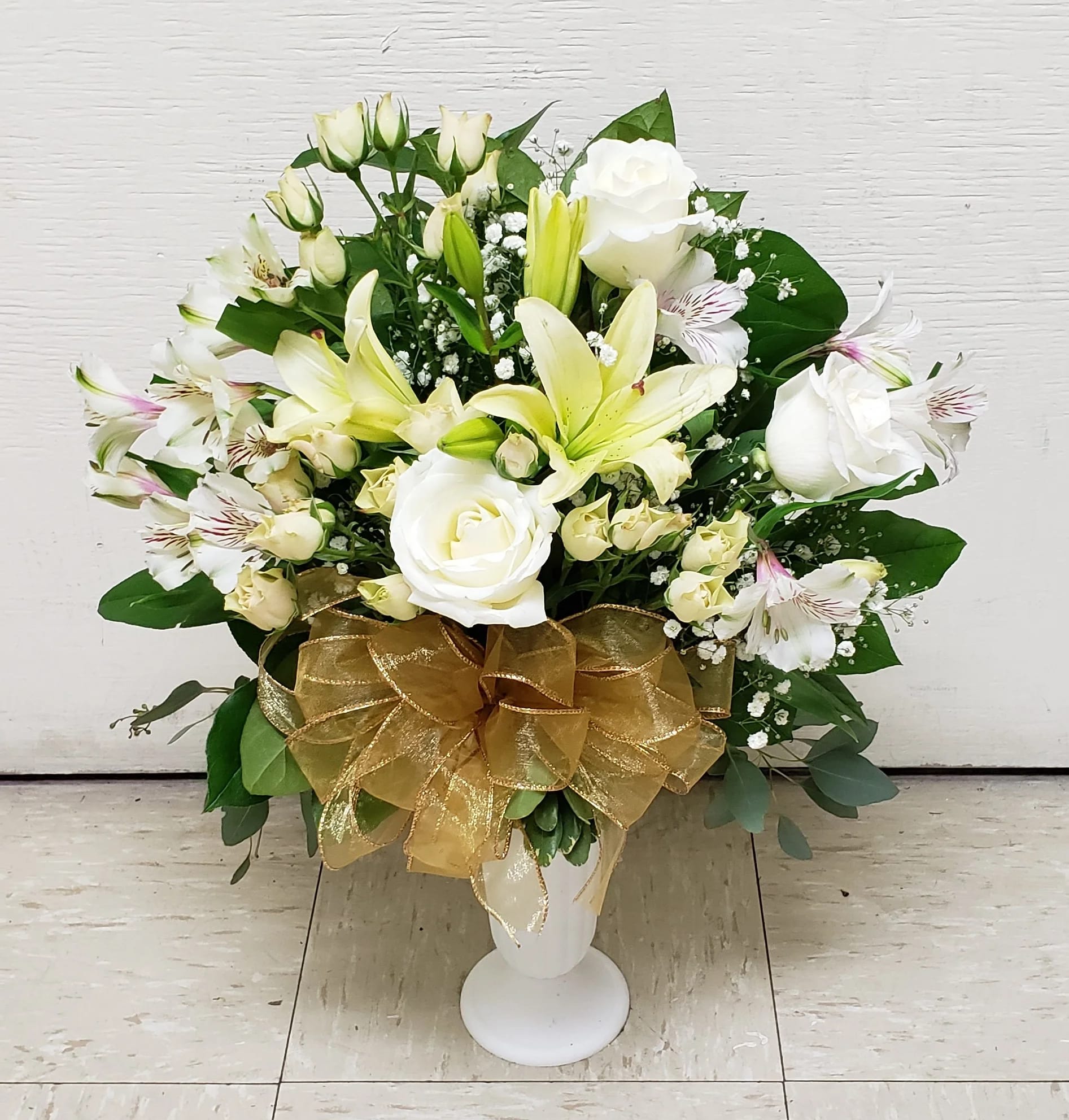 White roses and lilies arranged in a white vase with a gold bow