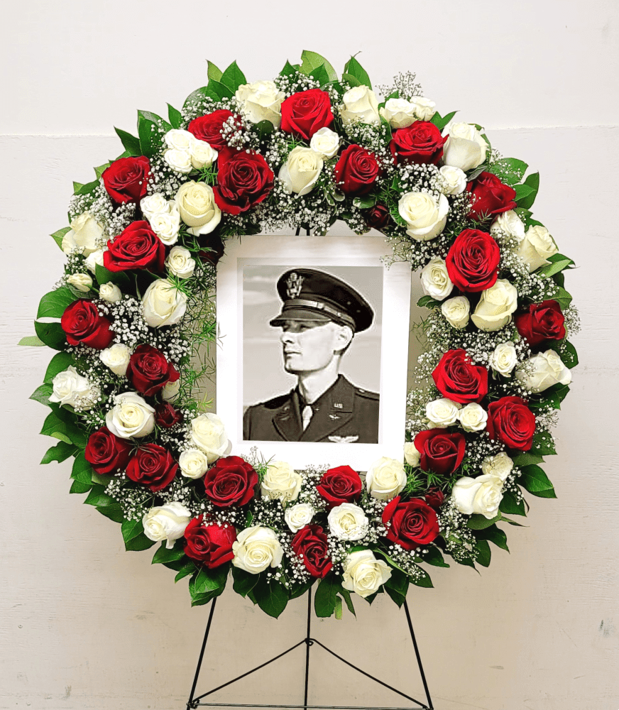 Standing wreath of red and white roses surrounding a central photo on an easel