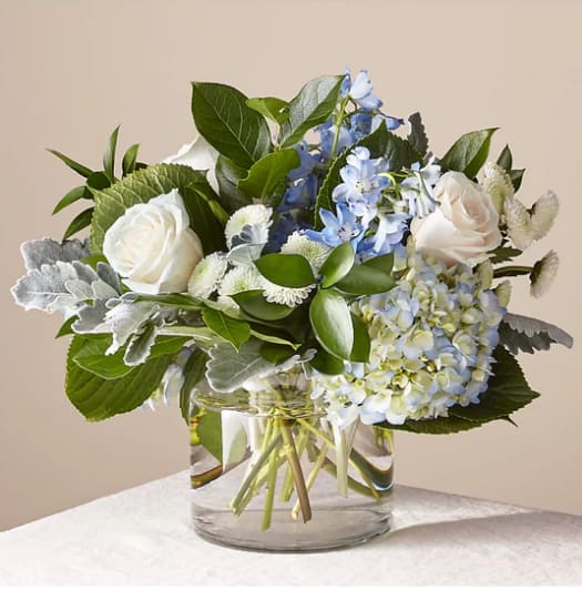 White roses and blue flowers in a clear glass vase