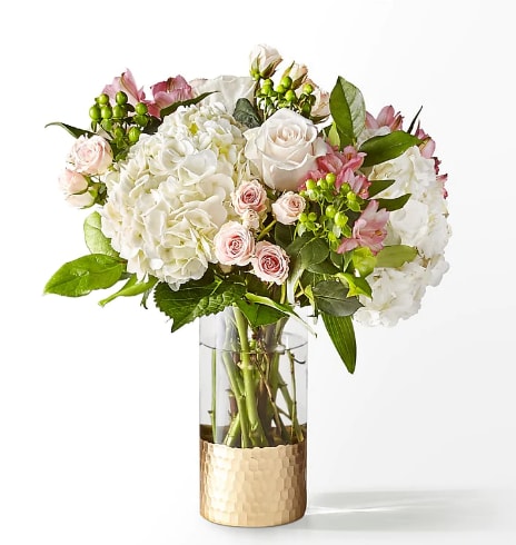 White and pink floral arrangement in a clear glass vase with a gold base