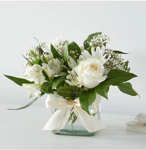 White rose and lily bouquet in a glass vase with a ribbon