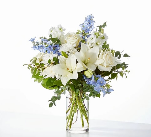 White lilies and roses with blue flowers in a clear glass vase