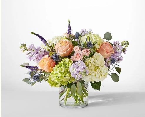 Peach roses and hydrangeas in a clear glass vase with lavender accents