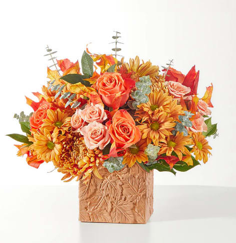 Orange and peach flowers in a leaf-patterned square vase