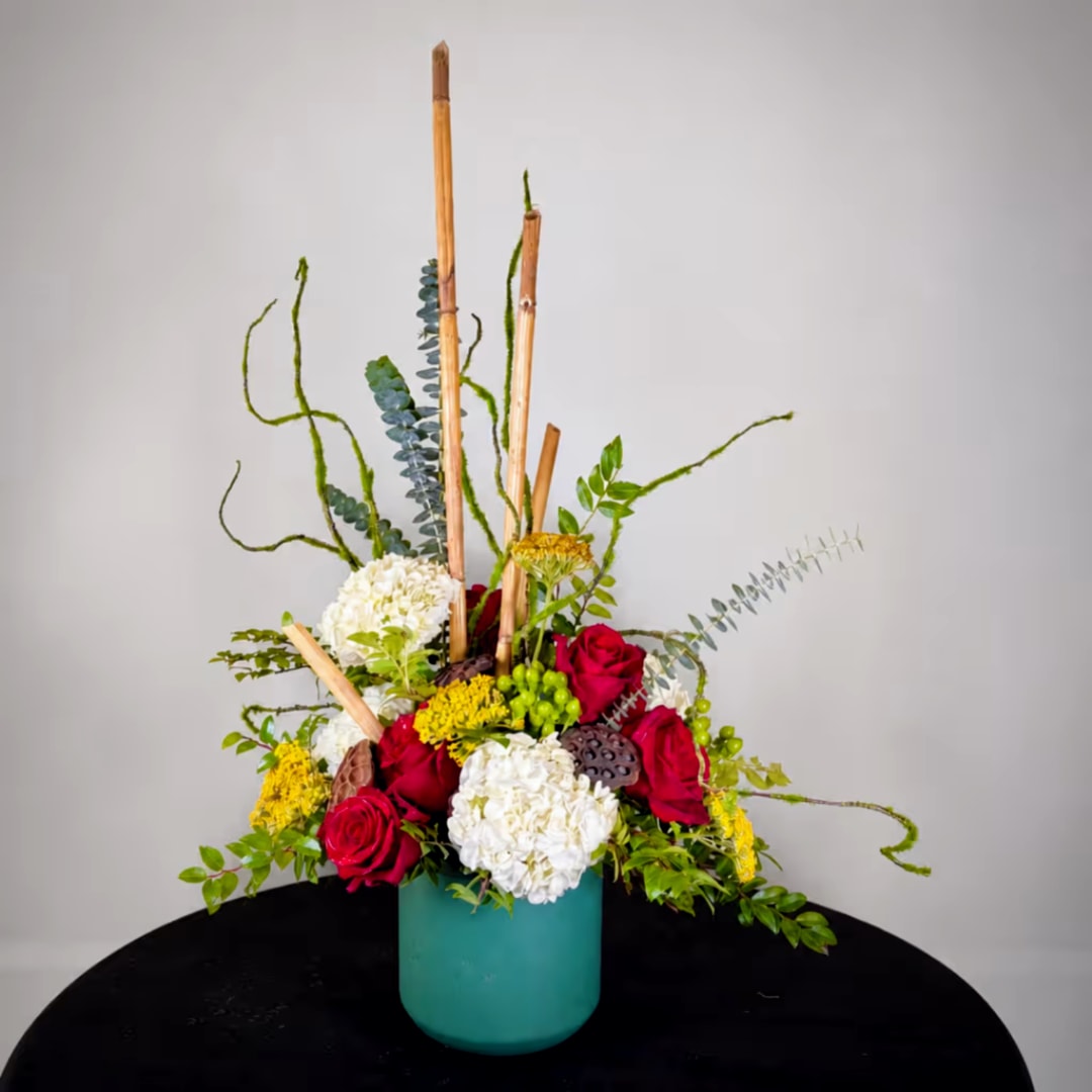 Tall floral arrangement in a teal vase with red, white, and yellow blooms