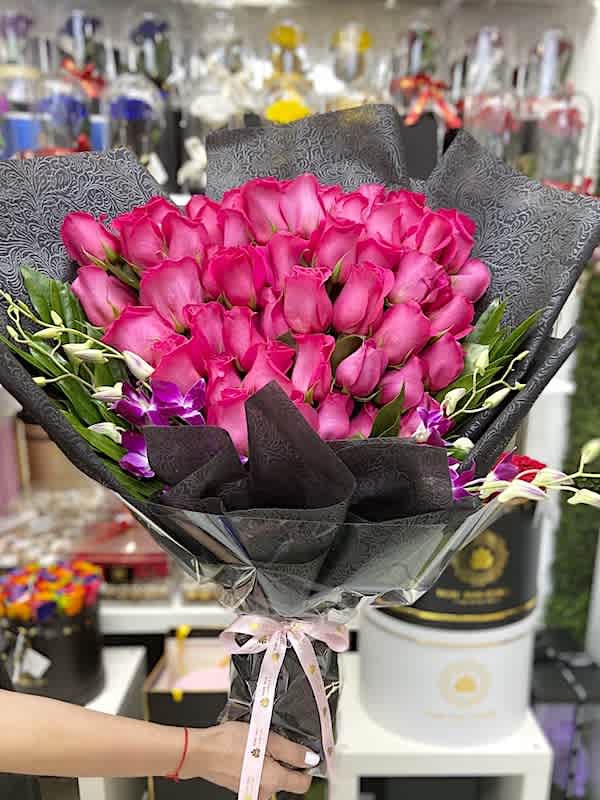 Large bouquet of bright pink roses with purple orchids wrapped in black paper.