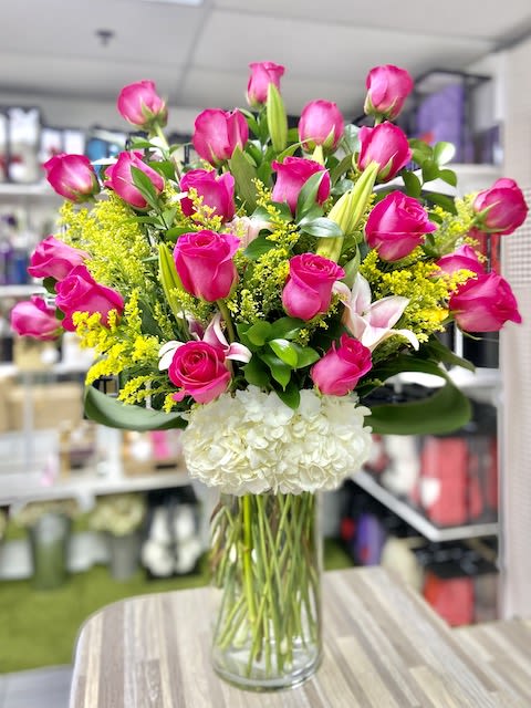 Tall glass vase of hot pink roses, lilies, and white hydrangeas with yellow filler flowers