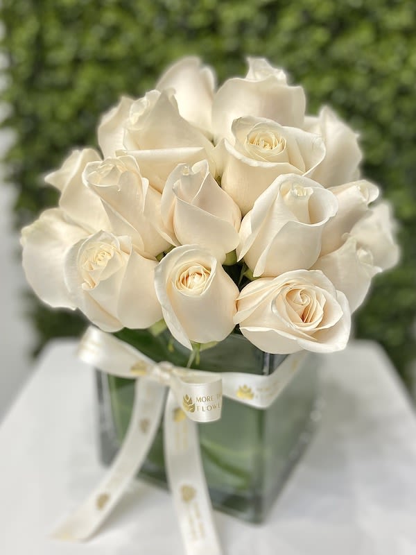 Compact arrangement of cream roses in a clear glass cube vase with a white ribbon bow