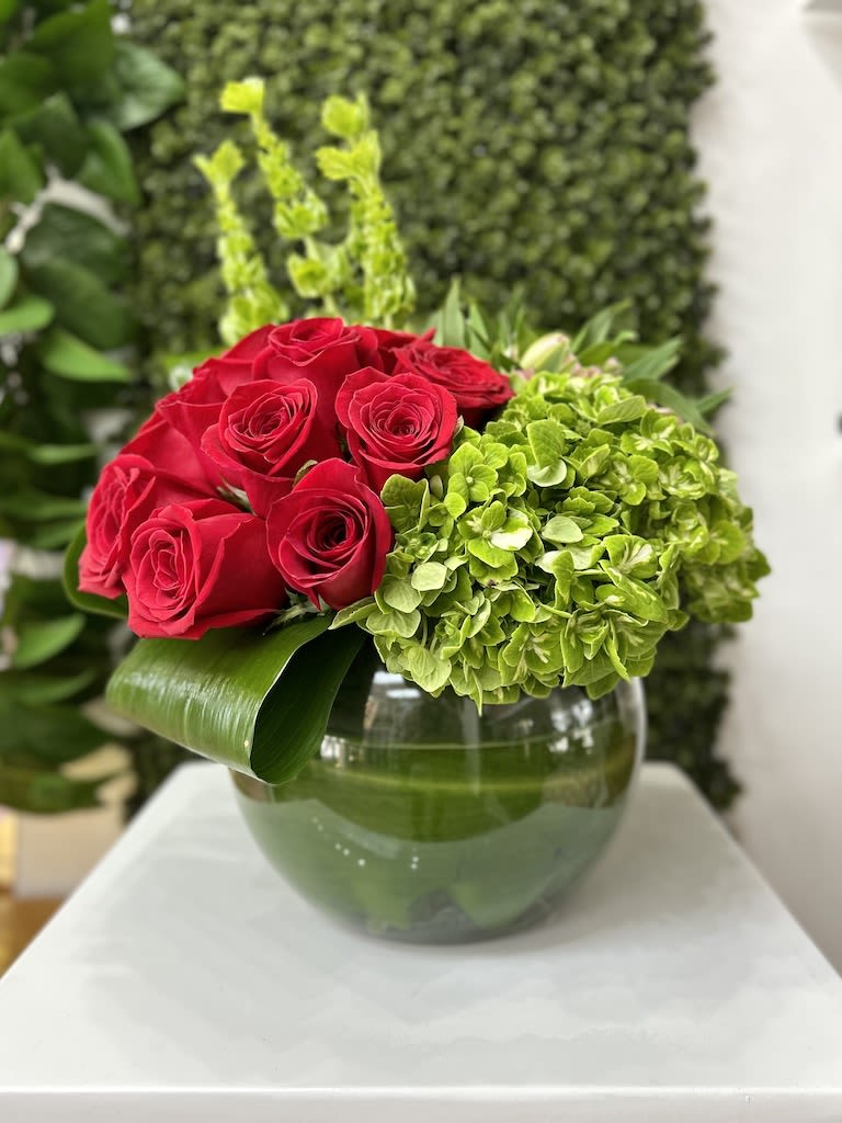 Low arrangement of red roses and green hydrangeas in a round glass vase