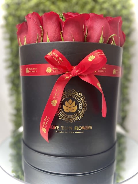 Round black hatbox filled with red roses and tied with a red ribbon bow