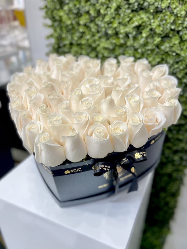 Heart-shaped black box filled with tightly packed ivory roses on a white pedestal