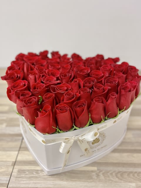 Heart-shaped white box filled tightly with red roses and tied with a cream ribbon