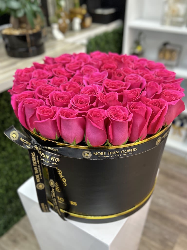 Round hatbox of bright pink roses in a black box with gold trim and ribbon