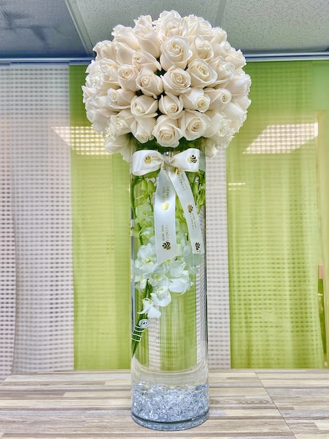 Tall glass cylinder vase with submerged white orchids topped by a dense dome of ivory roses and ribbon.
