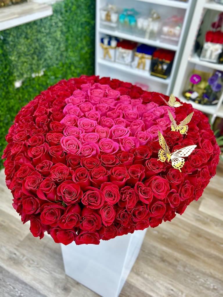 Heart-shaped arrangement of red and hot pink roses in a white box with gold butterfly accents