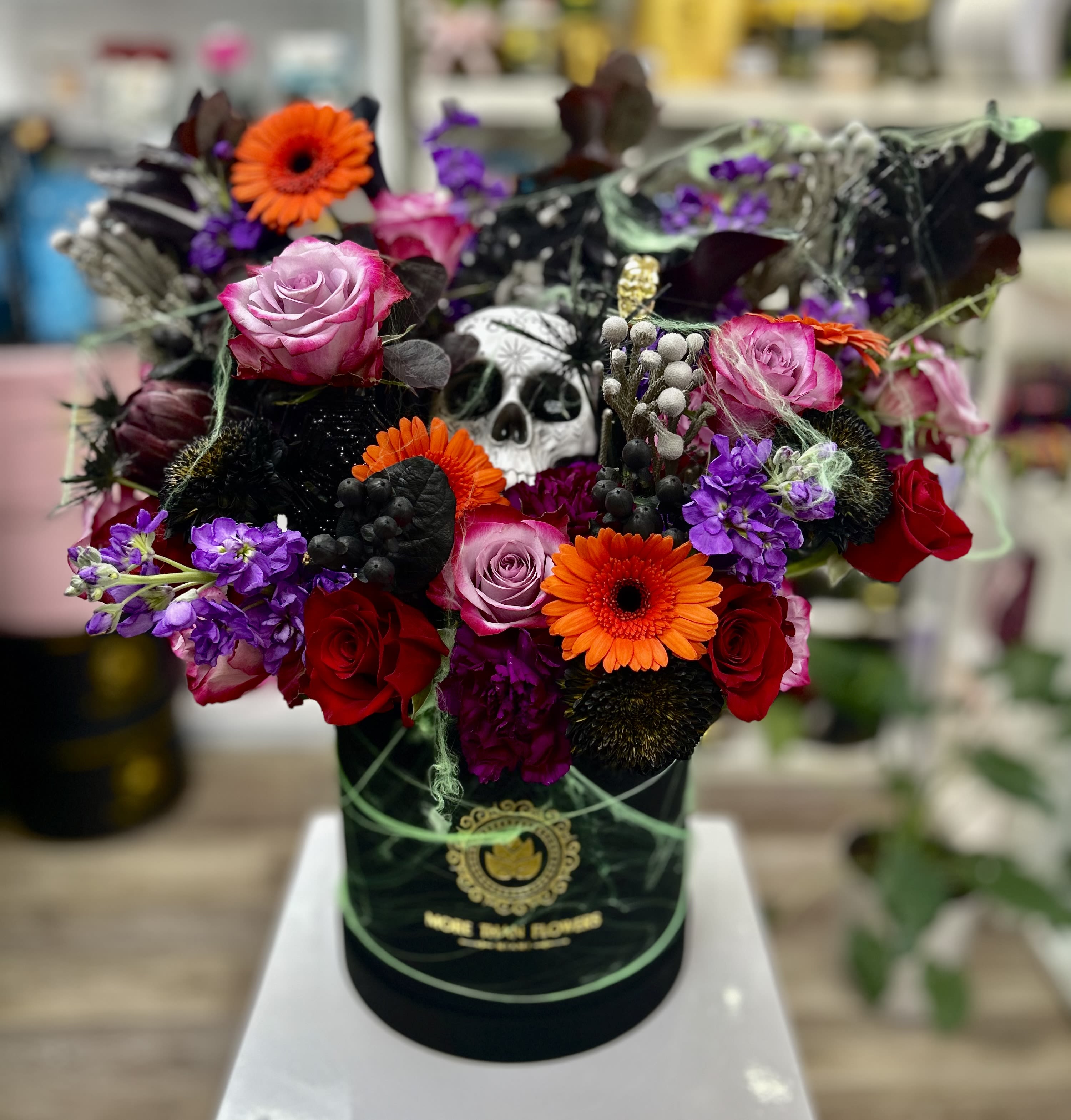 Halloween flower hatbox with bright roses, gerberas, purple blooms and a skull decoration.