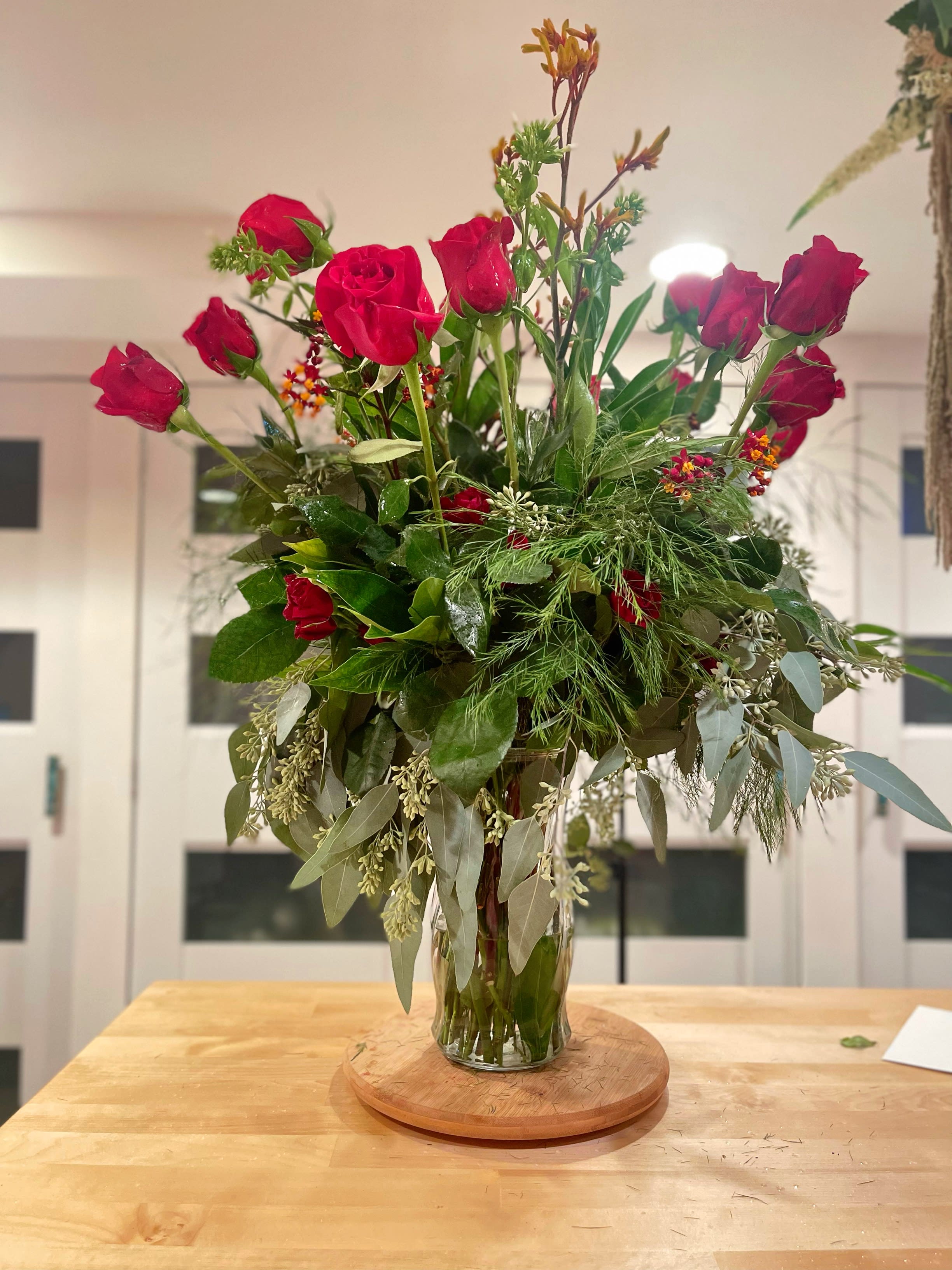 Tall vase arrangement of red roses with mixed greenery