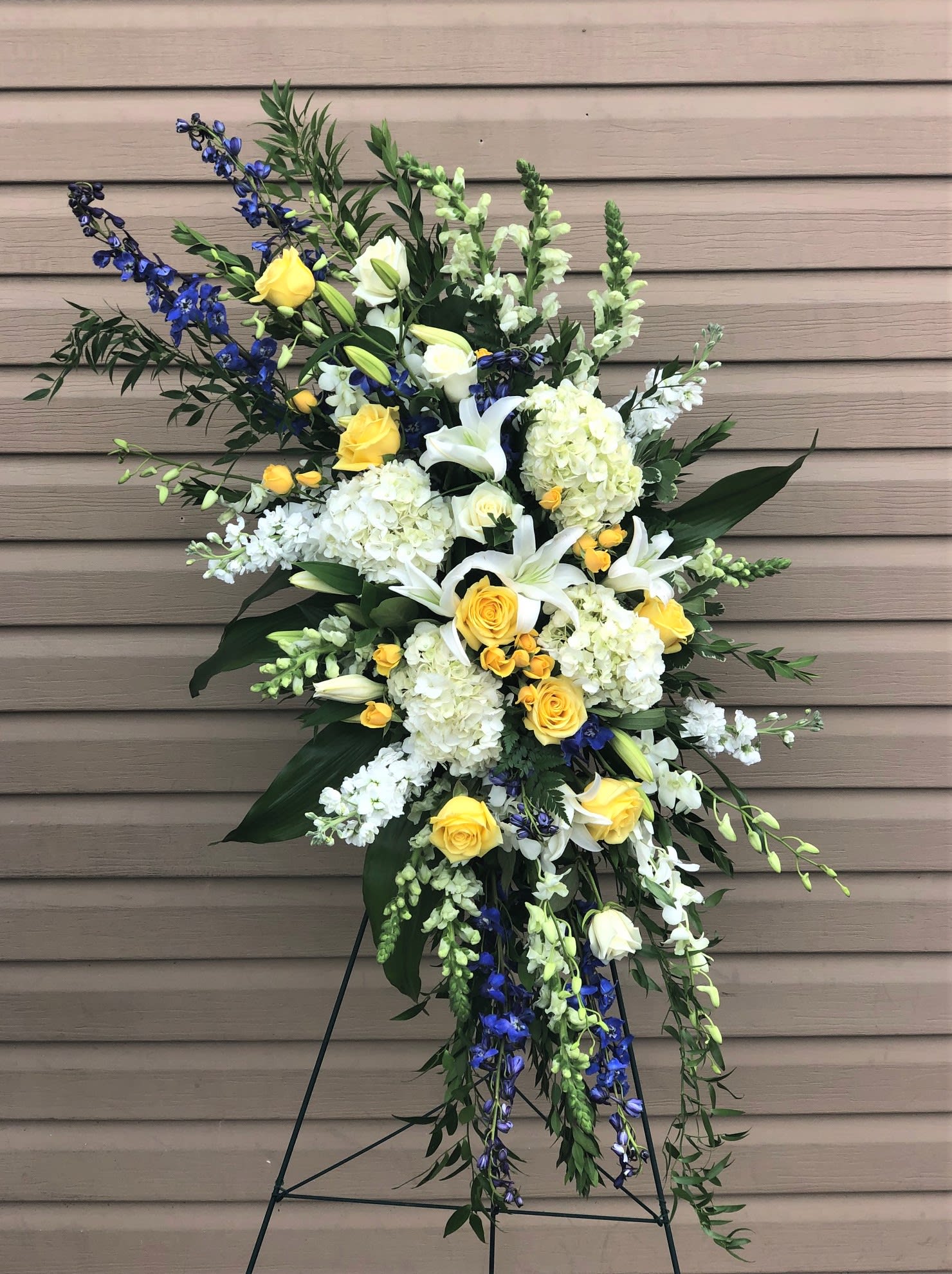 Standing floral spray with white lilies, yellow roses, and blue flowers