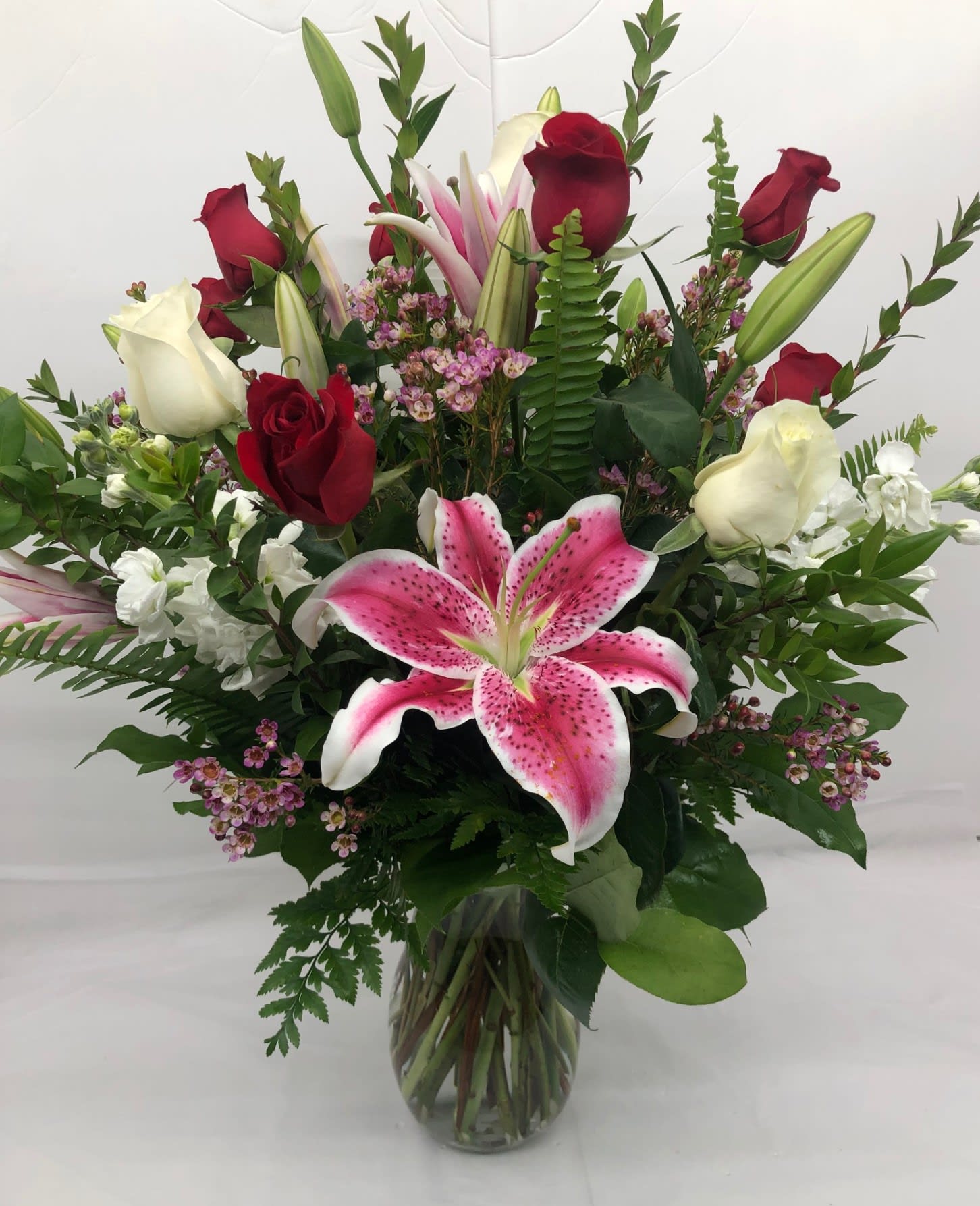 Mixed bouquet of pink lilies, red and white roses, and filler flowers in a clear glass vase