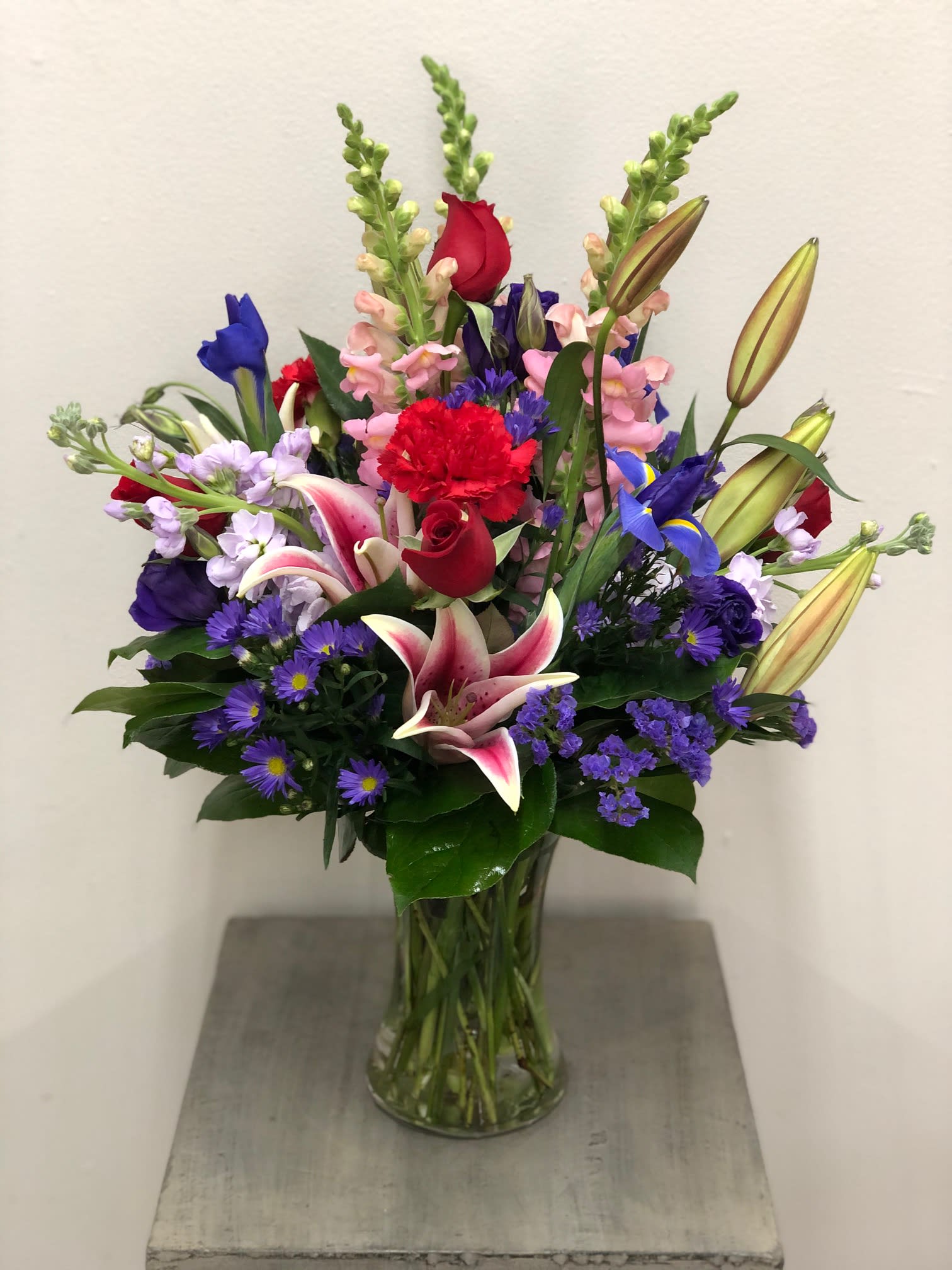 Mixed bouquet of lilies, roses, and purple filler flowers in a glass vase