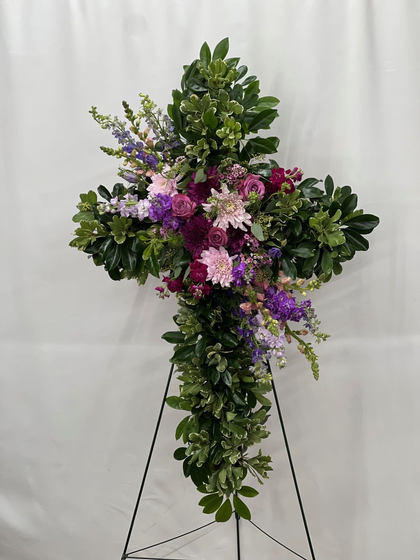 Large cross-shaped floral tribute with purple and pink flowers on a stand