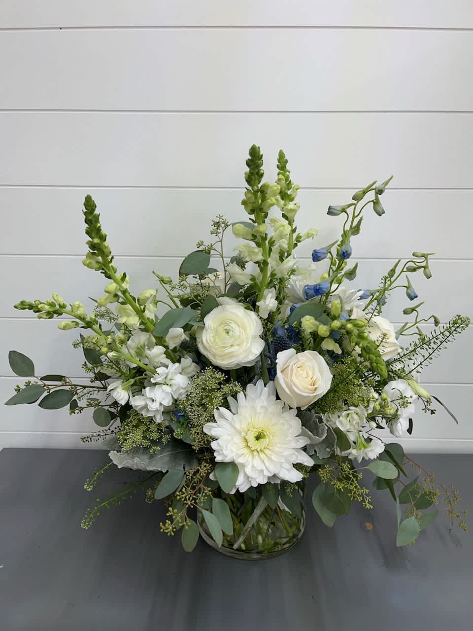 White roses and daisies in a glass vase with blue accents