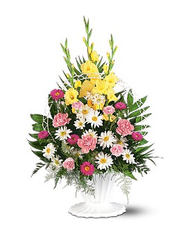Standing floral spray with yellow, pink, and white flowers in a white pedestal vase