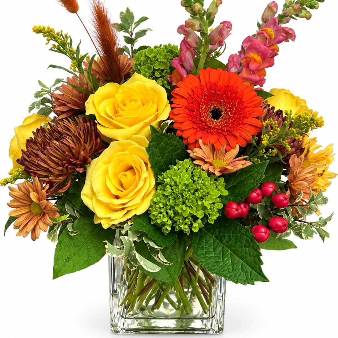 Mixed bouquet of yellow roses, orange gerbera daisies, and chrysanthemums in a glass vase