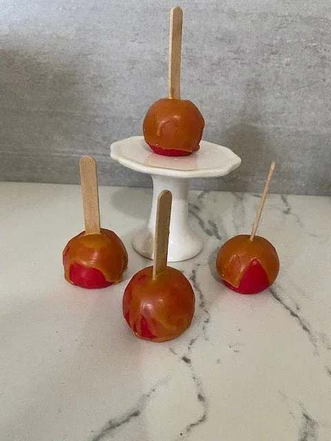 Four caramel apples on sticks, arranged around a small white pedestal stand