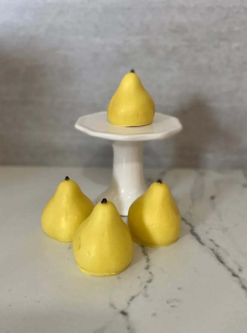 Four yellow pear-shaped objects on a white pedestal stand