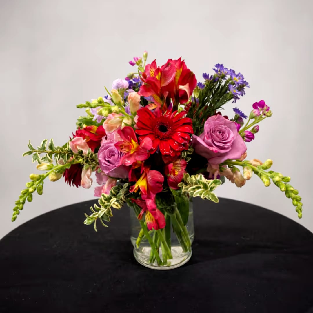 Mixed bouquet of red, pink, and purple flowers in a clear glass vase