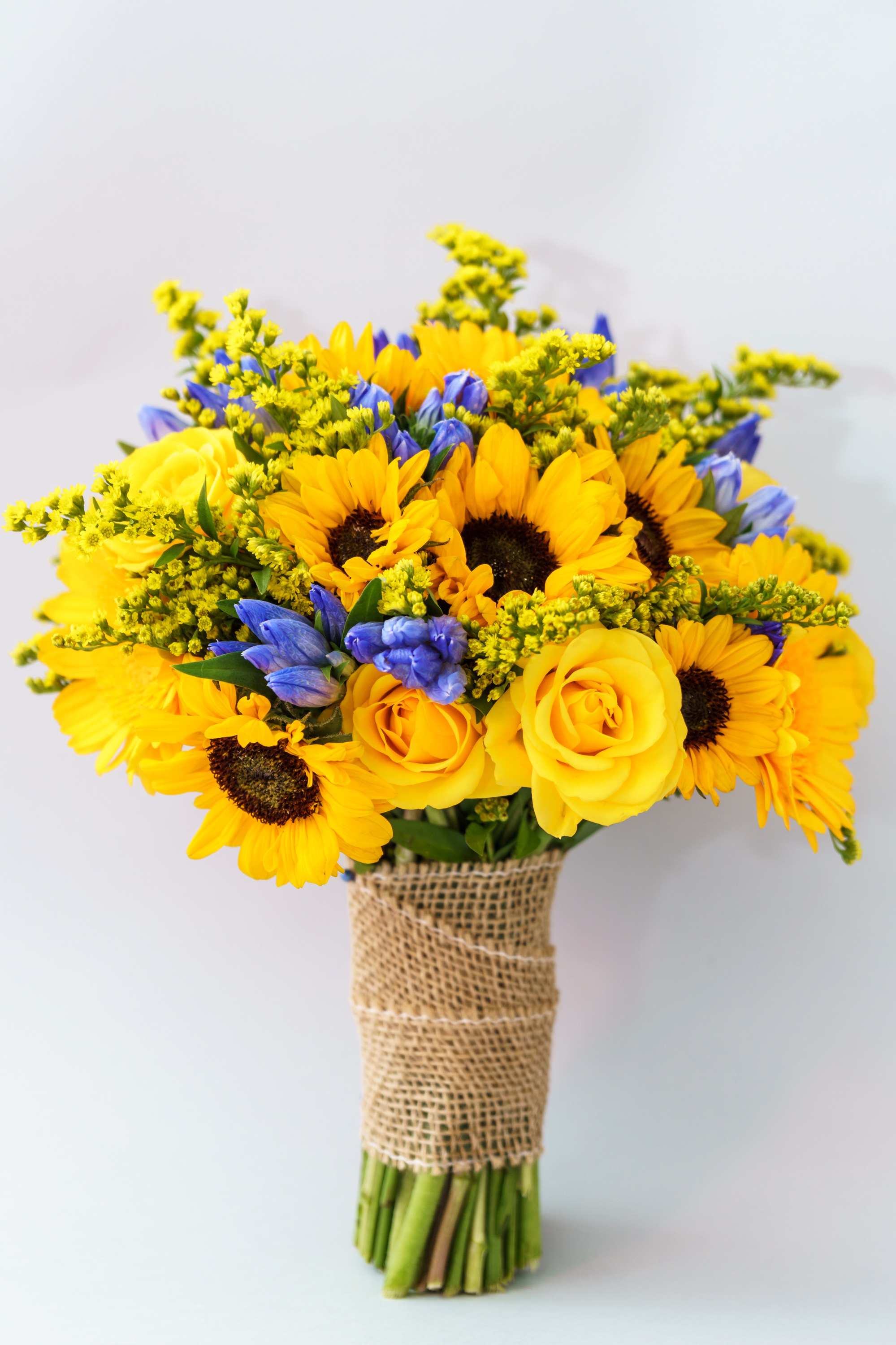 Bouquet of yellow sunflowers and roses with blue flowers wrapped in burlap