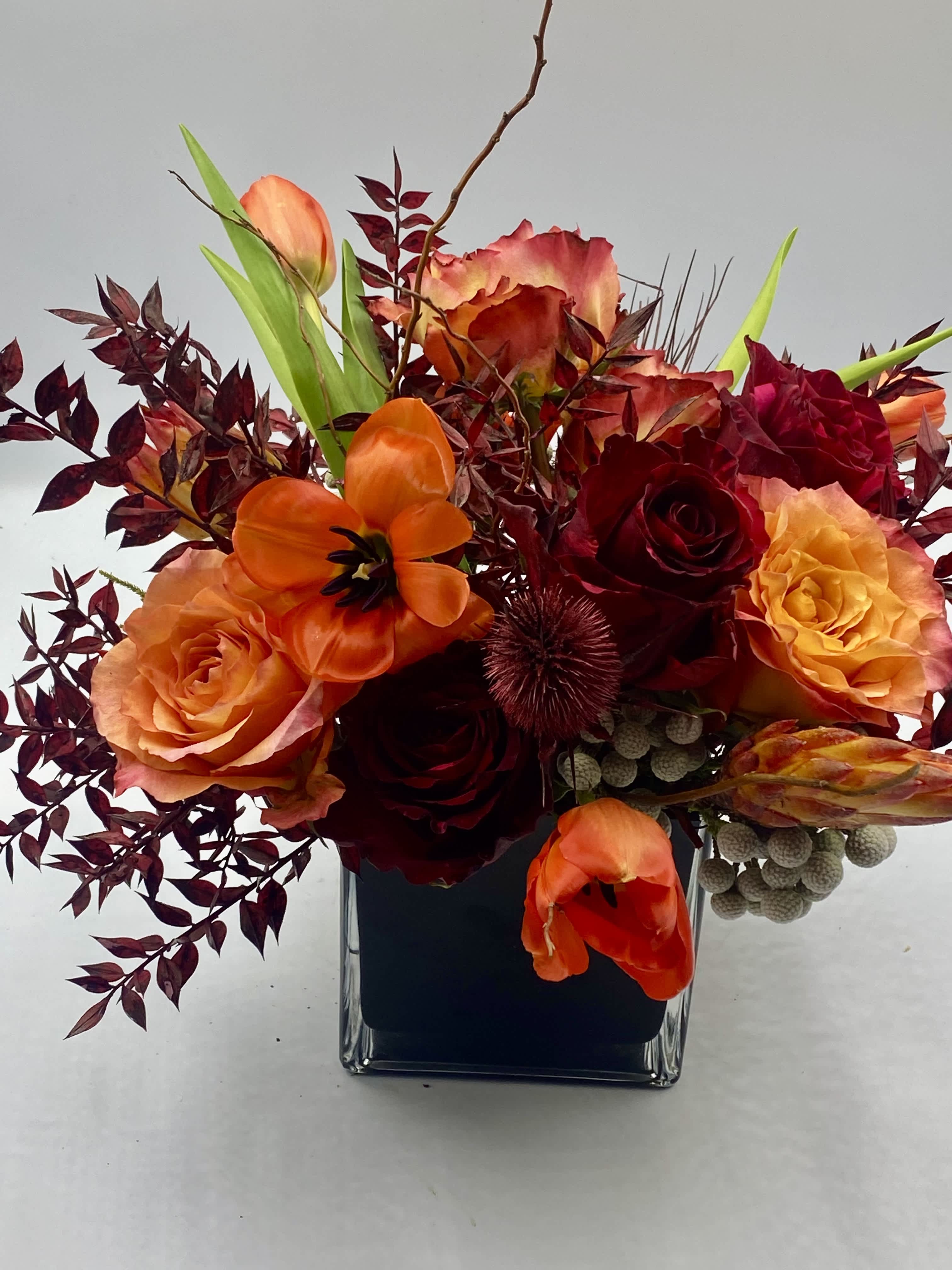 Orange and red roses with tulips in a square glass vase
