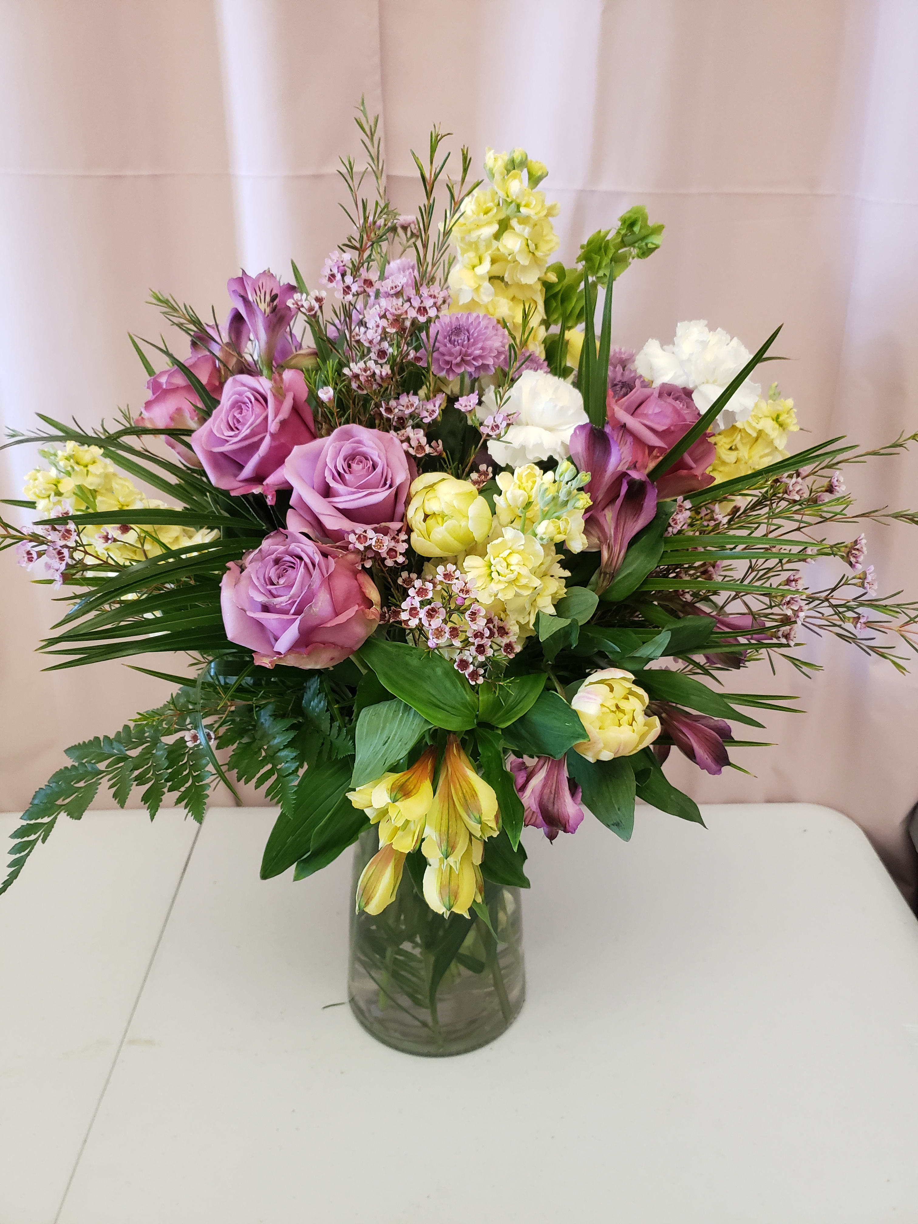 Lavender roses and yellow flowers arranged in a glass vase