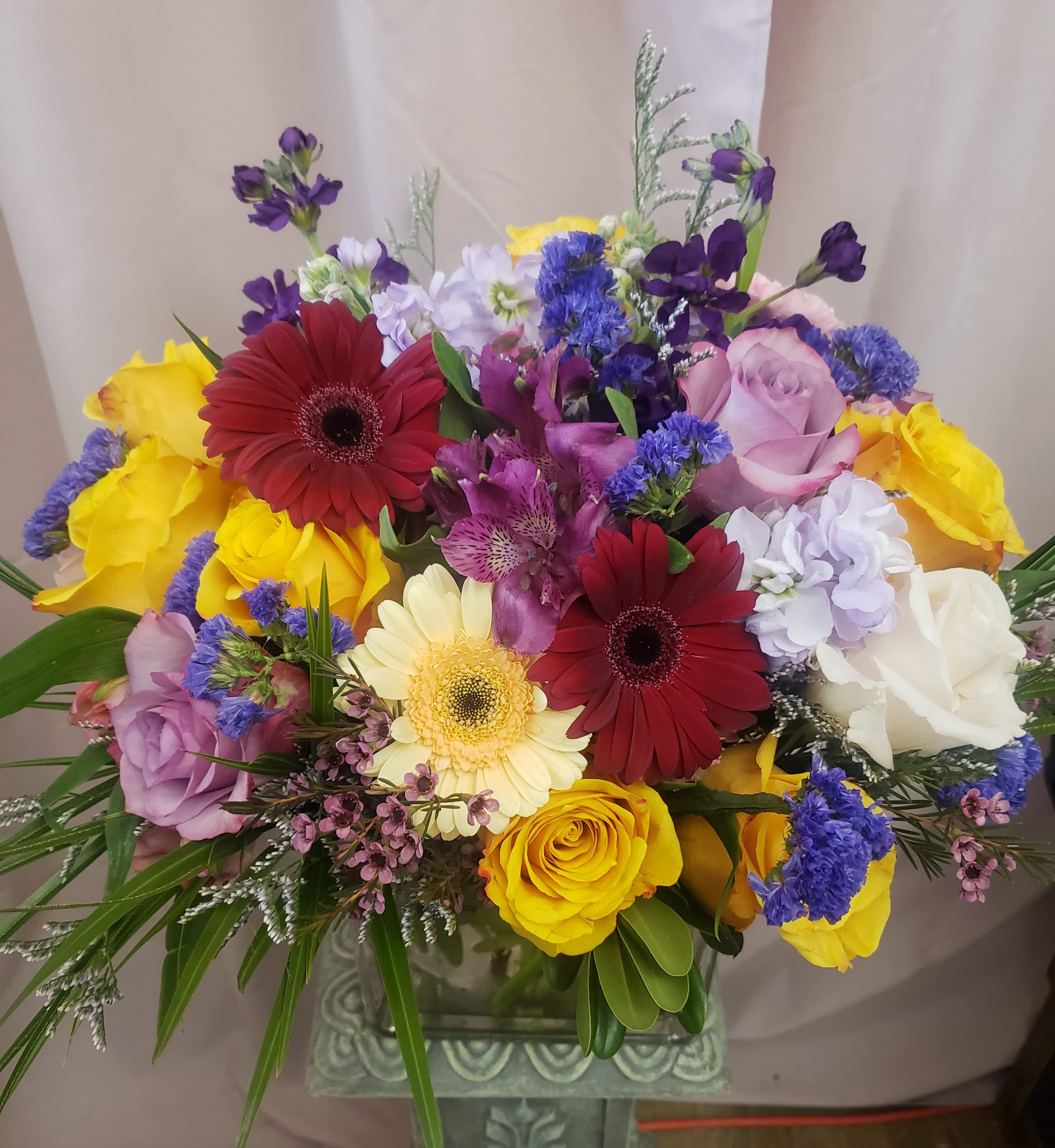 Mixed bouquet of roses, gerbera daisies, and purple filler flowers in a vase