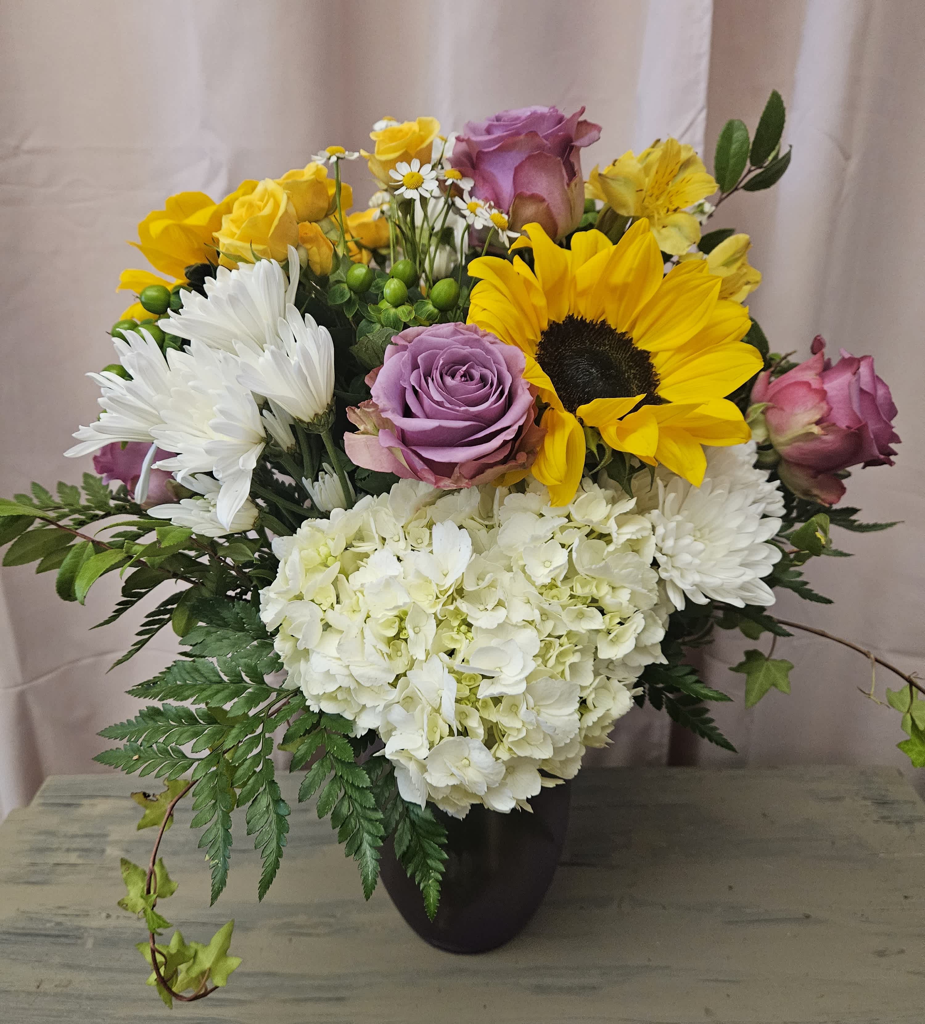 Bouquet of sunflowers, roses, daisies, and white hydrangeas in a dark vase