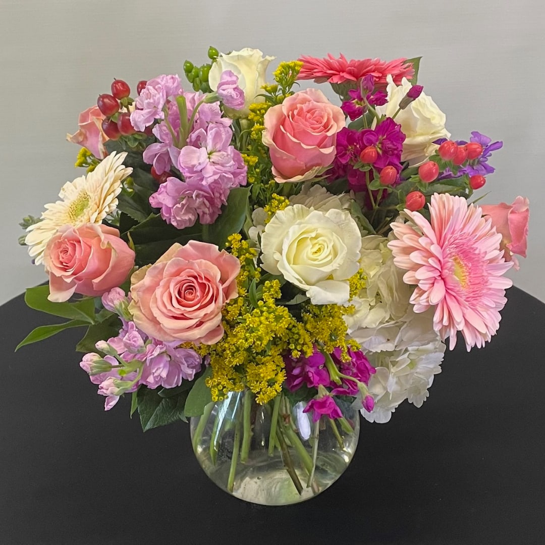 Mixed bouquet of pink, white, and purple flowers in a clear glass vase