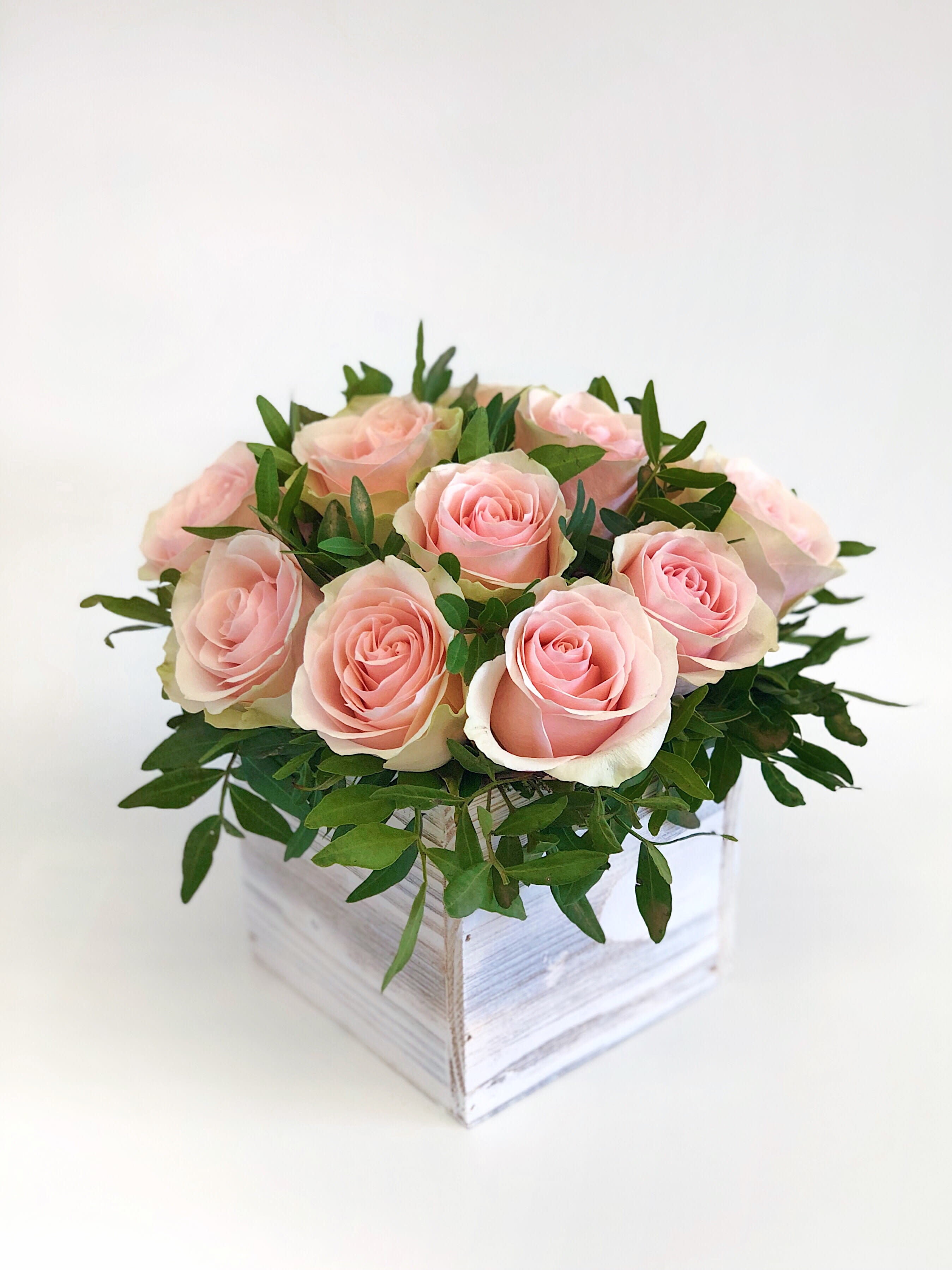 Pink roses arranged in a white wooden box with greenery