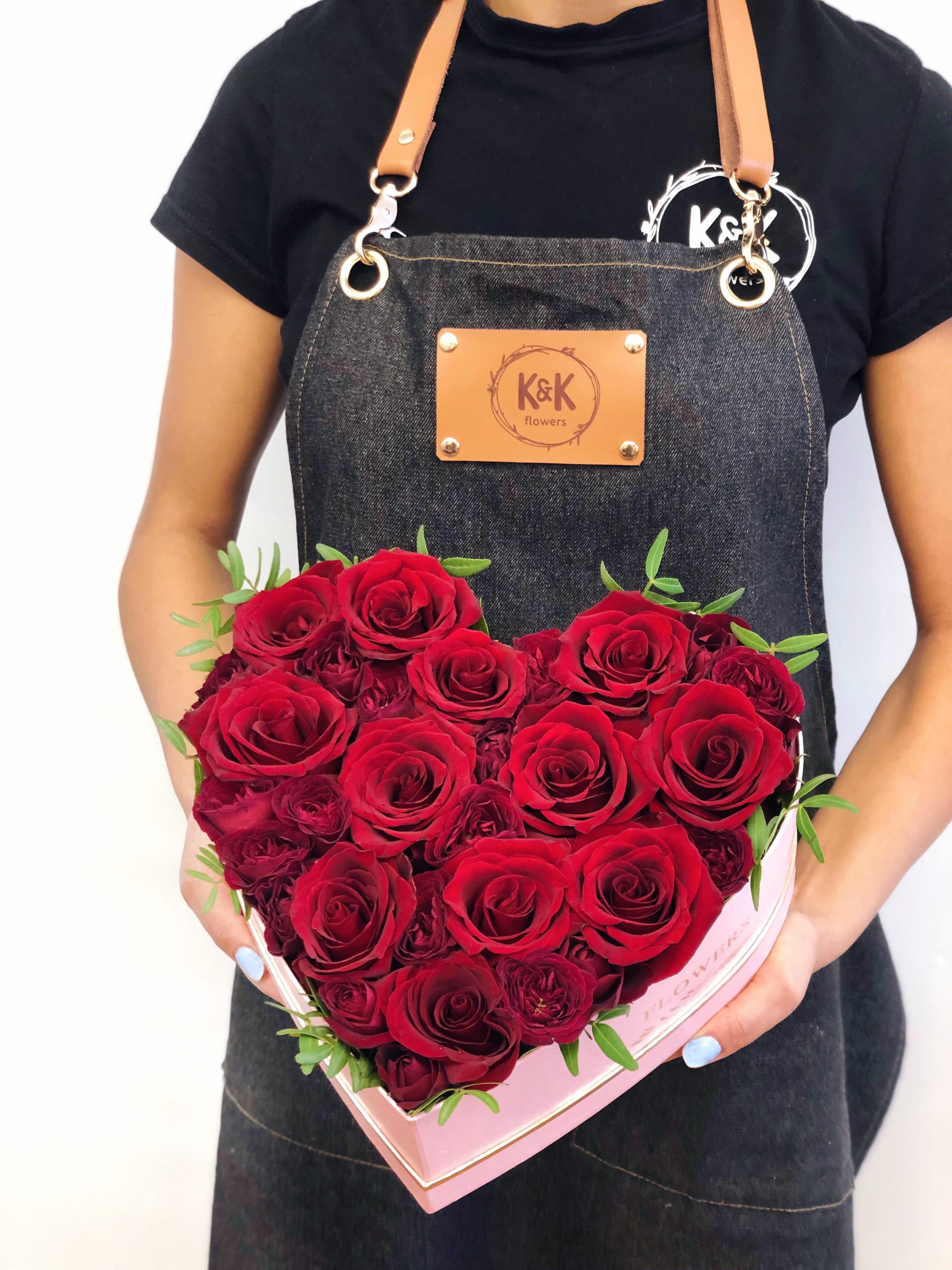 Heart-shaped box of red roses held by a person in an apron
