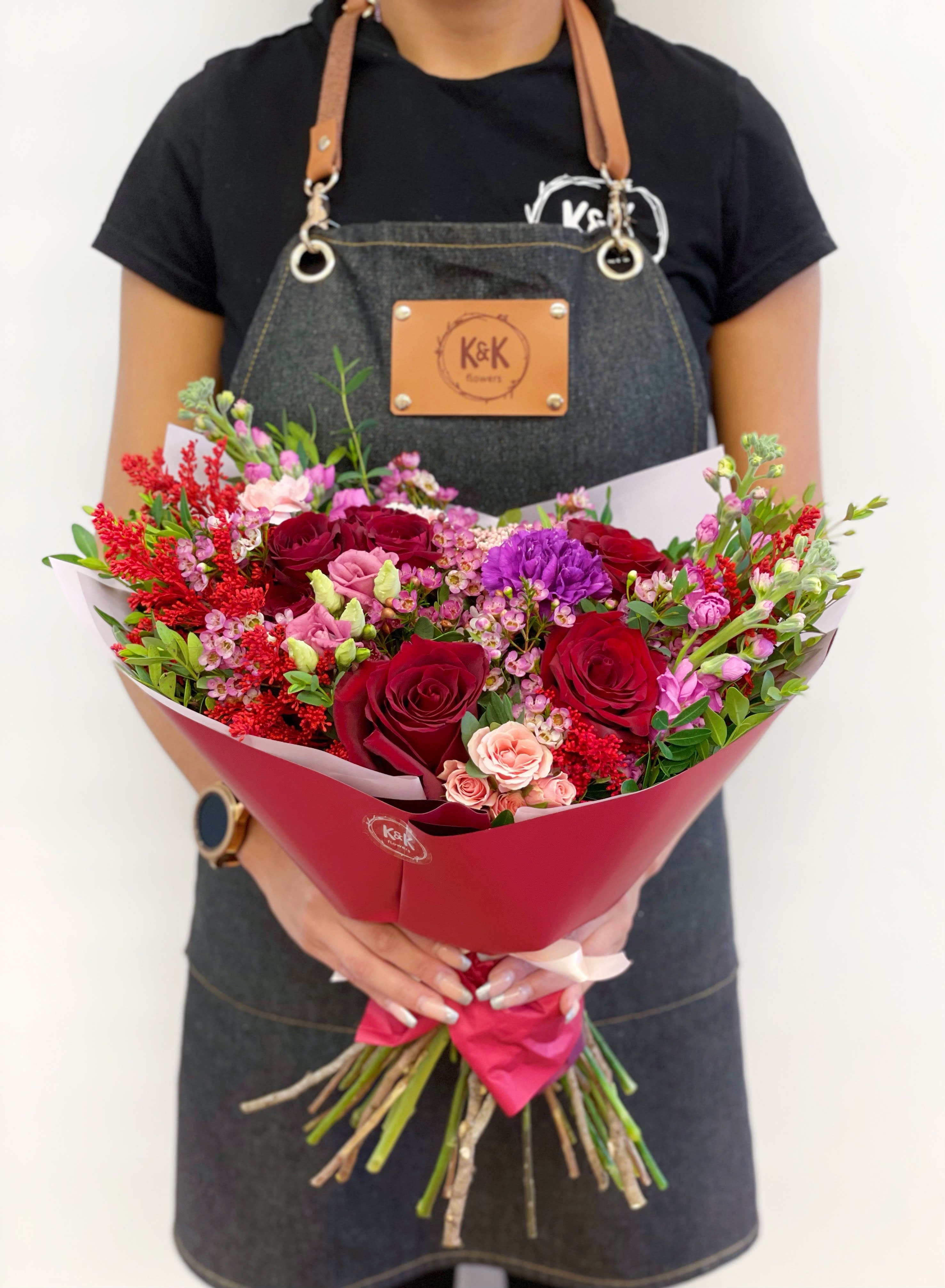 Handheld bouquet of red, pink, and purple roses with mixed filler flowers