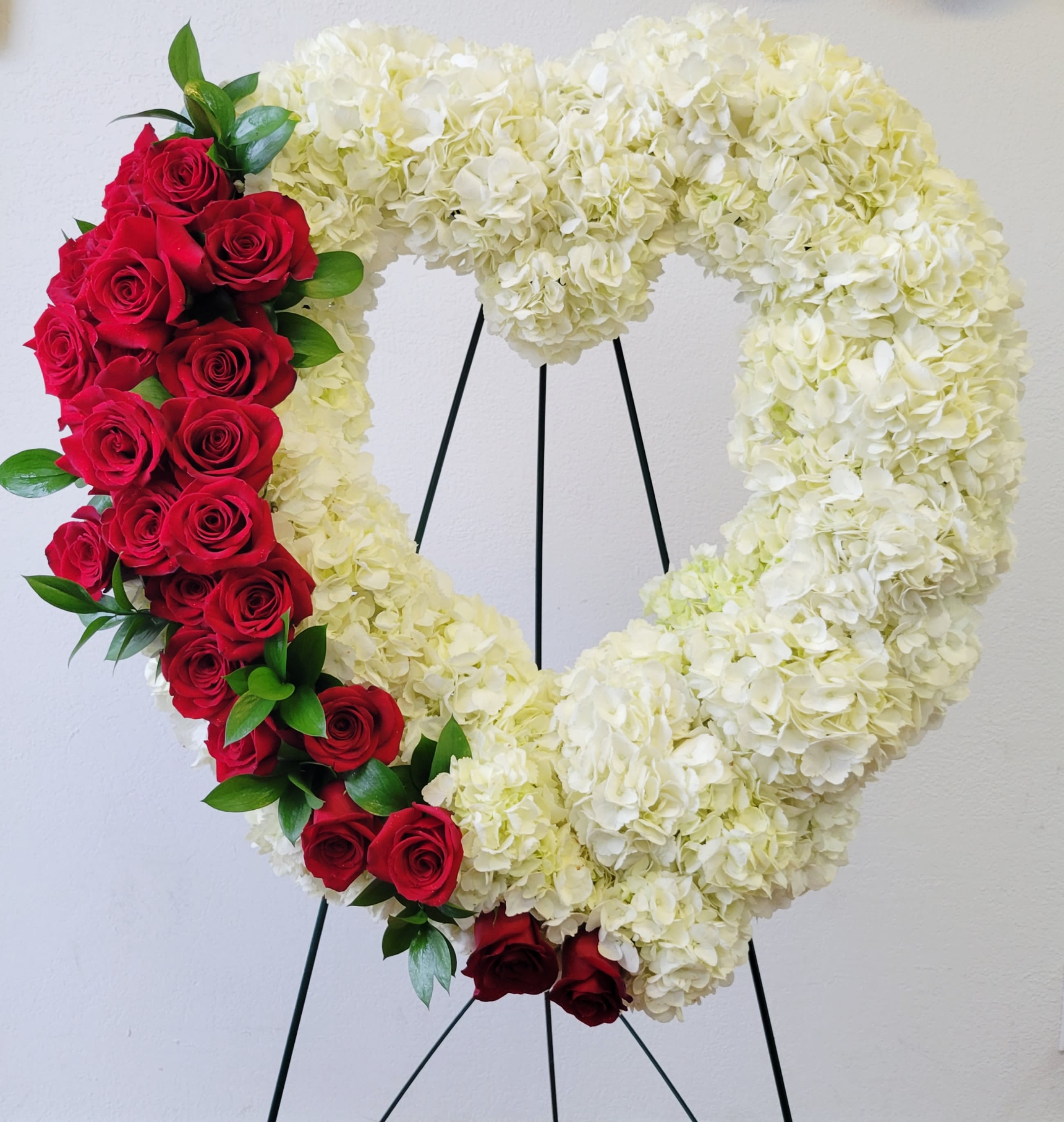Heart-shaped floral wreath with white hydrangeas and red roses on a stand