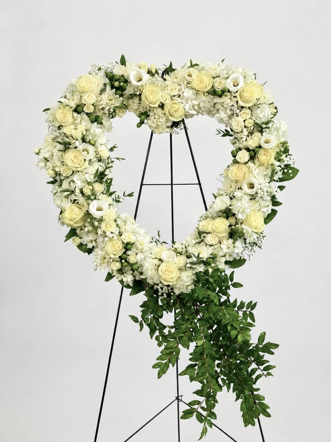 Heart-shaped floral wreath of white and pale yellow flowers on a black stand
