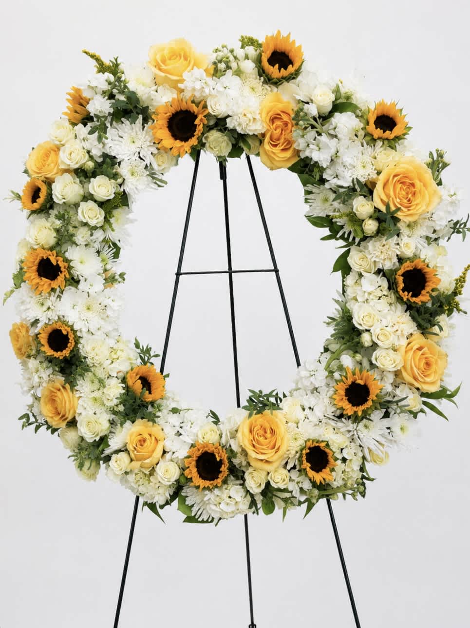 Heart-shaped floral wreath with yellow roses, white flowers, and sunflowers on an easel